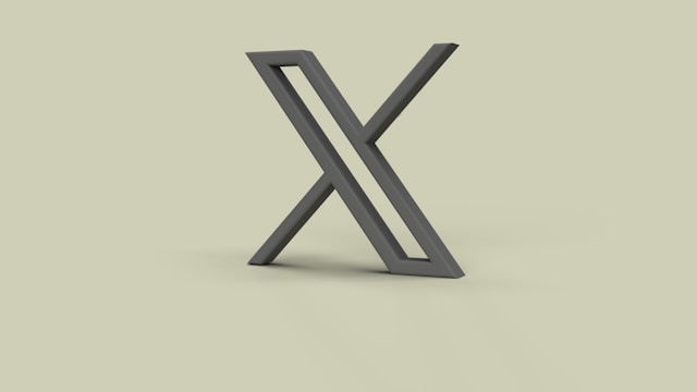A minimalistic, three-dimensional black "X" symbol standing upright on a light beige background.