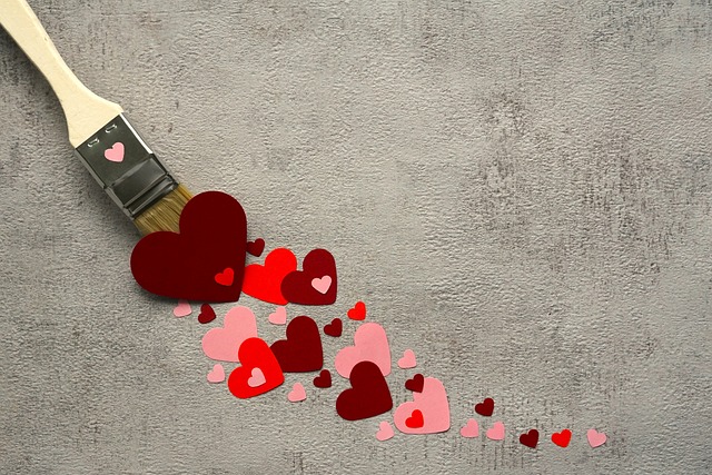 A paintbrush is shown "painting" various red and pink paper hearts onto a textured gray surface, creating a trail of hearts.