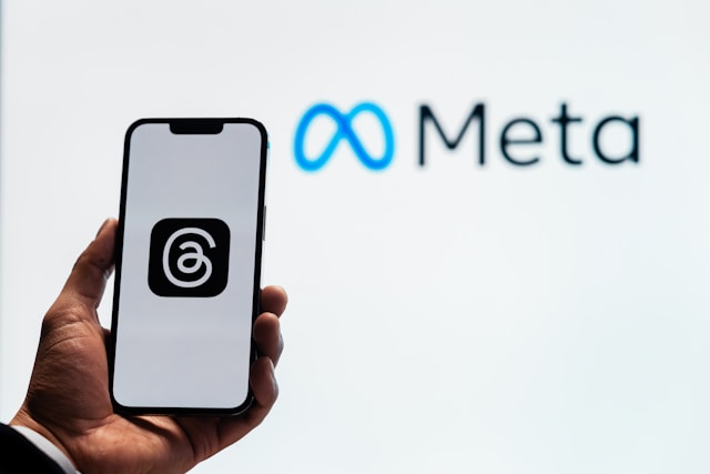 A hand holding a phone displaying the Threads app logo, with the Meta logo in the background.