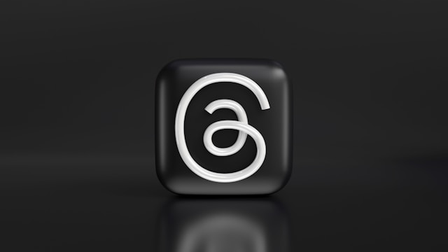 A black cube with the Threads logo on a dark background, giving it a sleek and minimalist appearance.