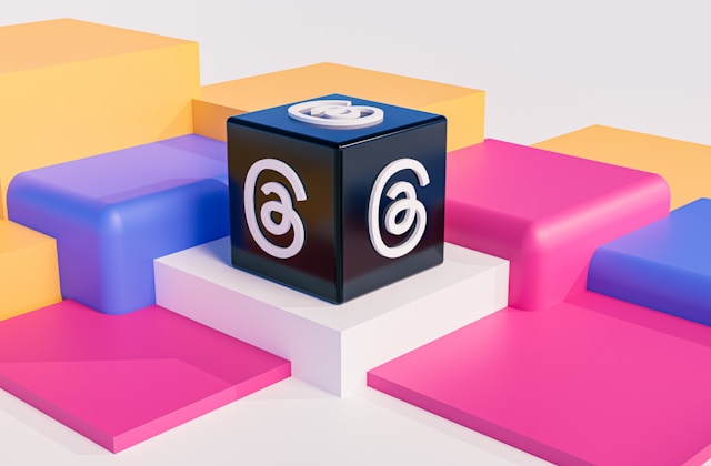 A black cube with the Threads logo on multiple sides, placed on colorful geometric platforms.