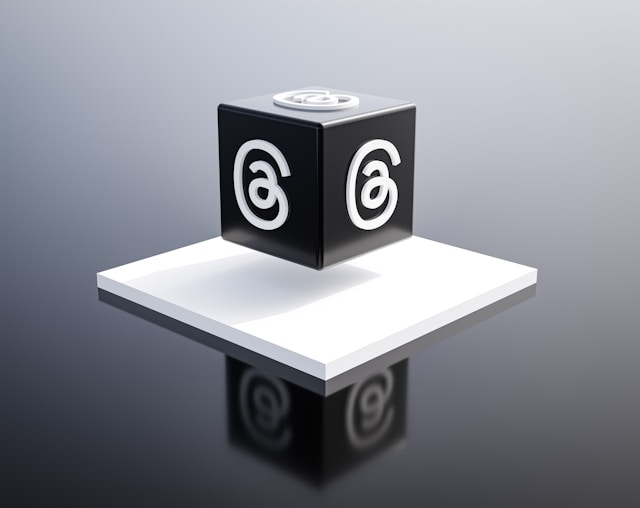 A black cube with the Threads logo on a reflective surface, positioned on a white platform.