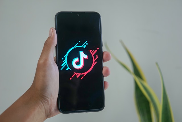 A hand holding a smartphone displaying the TikTok logo on the screen.