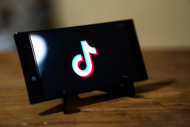 A smartphone screen displaying the TikTok logo, propped up on a wooden surface.