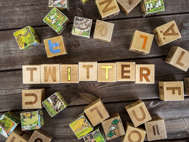 Wooden blocks spelling "TWITTER" arranged on a wooden surface, surrounded by colorful letter and image blocks.