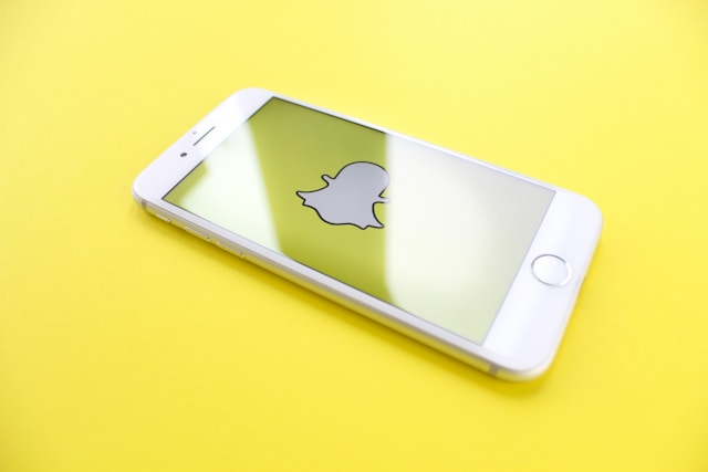 A smartphone displaying the Snapchat logo on its screen, placed on a bright yellow surface.